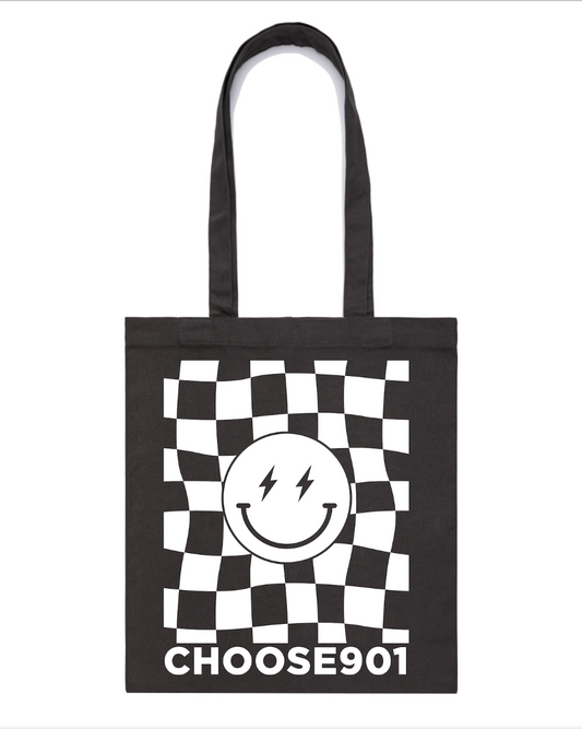 Black tote bag with a checkered border, featuring a central graphic of a smiling face with lightning bolt eyes and the text “choose901” below. This Choose901 Merch Shop Tote Bag combines style and functionality