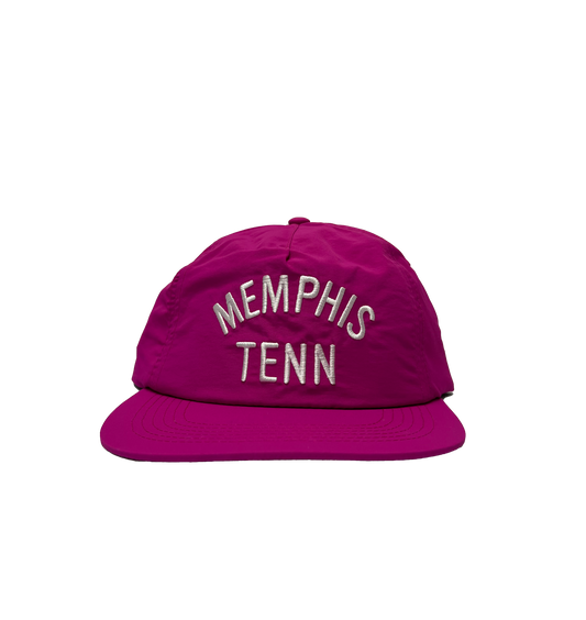 A red snapback cap embroidered with "Memphis Tenn" in white letters, displayed against a striped background.