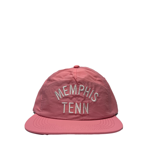 A pink snapback cap with "memphis tenn" embroidered in white thread, displayed against a striped pink and gray background. 
could be rephrased as:
A Memphis Tenn Pink Nylon Hat by Choose901 Merch Shop with "memphis tenn" embroidered in white thread, displayed against a striped pink and gray background.
